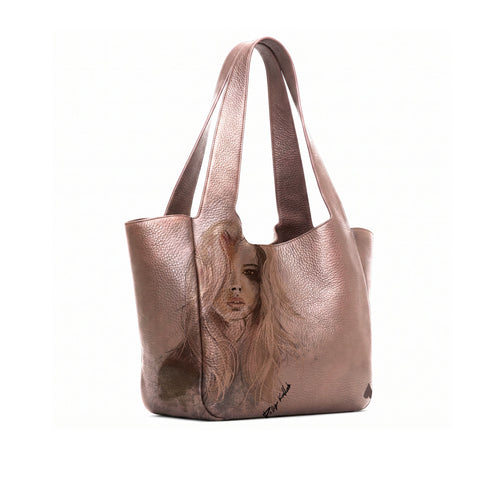 A Bronze leather tote bag featuring a painted portrait of a woman on the front, set against a plain white background.