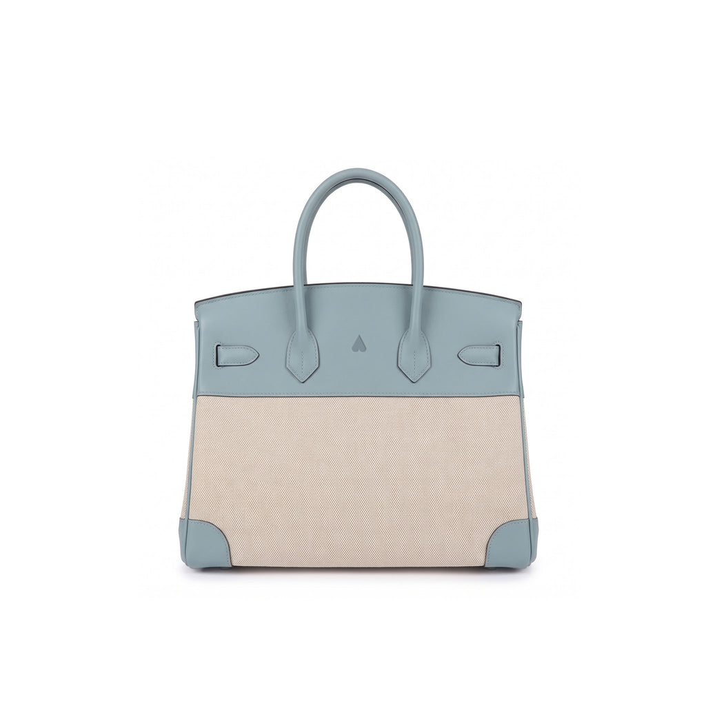 A structured leather handbag with a colorblock design, featuring a dusty blue top section and handles, and a beige canvas lower body, shown against a plain white background.