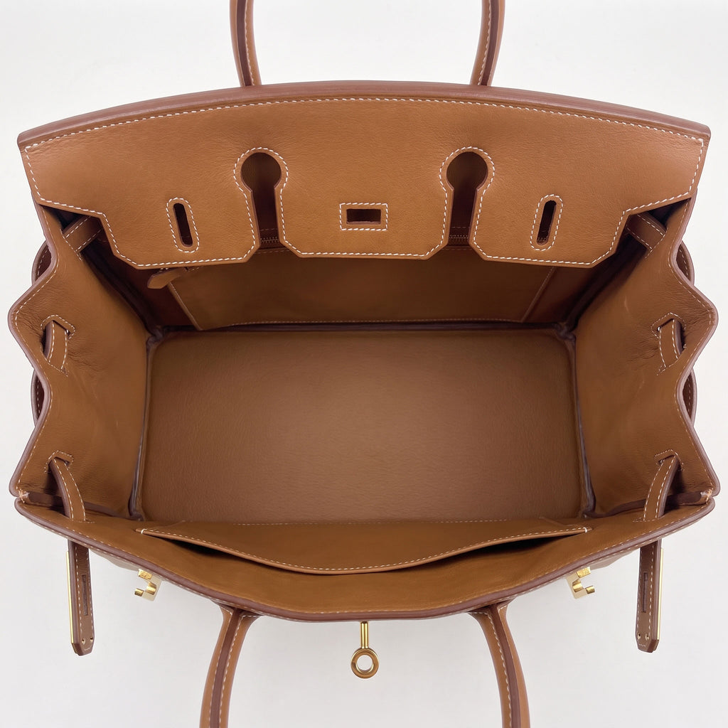 A top-down view of a brown leather handbag interior, showing the spacious main compartment, lining, and gold-tone hardware on a plain white background.