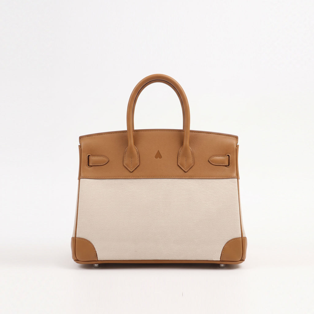 A structured leather handbag with a tan top panel and handles, a light beige woven body, and tan corner protectors, photographed against a plain white background.