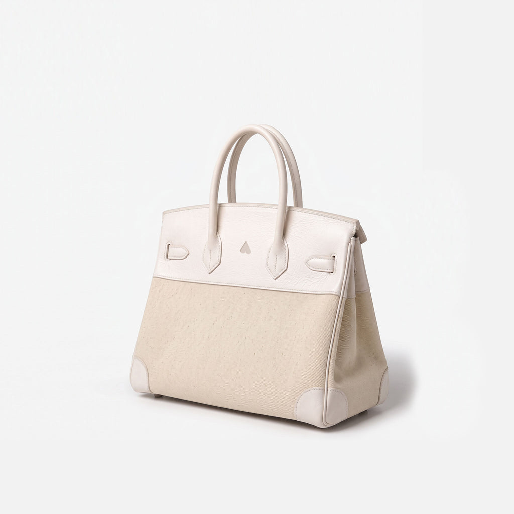 A structured handbag in light beige and off-white leather, featuring dual top handles, a triangular metal logo detail on the front, and protective corner patches, set against a plain white background.