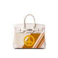 A structured cream-colored leather handbag with silver-tone hardware, featuring a yellow peace sign graphic and diagonal orange and white stripes on the lower front panel, set against a plain white background.
