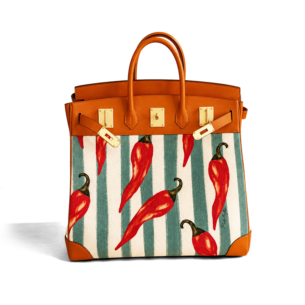 A structured leather handbag with a warm tan/cognac finish, featuring a front panel printed with large red chili peppers over vertical cream and teal stripes. The bag has gold-tone hardware and double top handles, photographed on a clean white background.