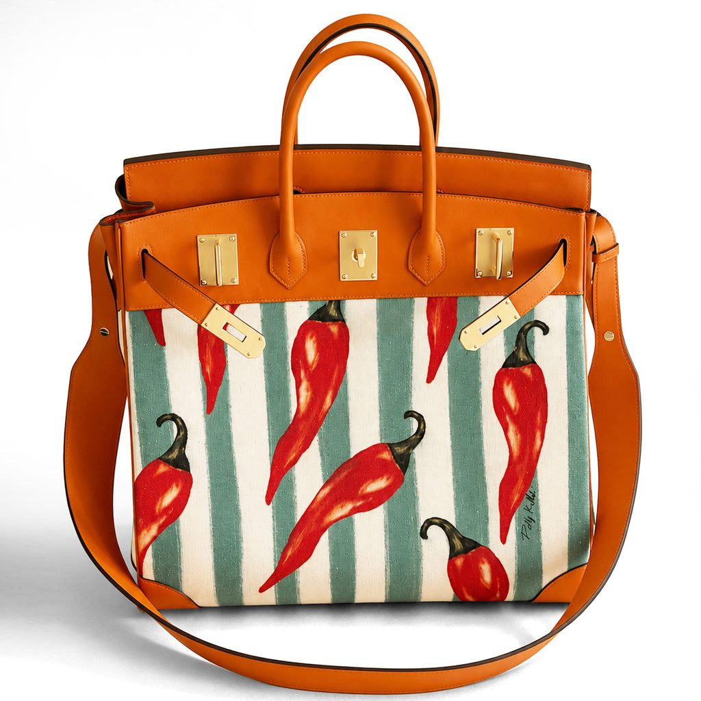 A structured leather handbag with a warm orange-brown leather trim and handles, featuring a front panel printed with red chili peppers on a white and teal-green striped background. The bag has gold-tone hardware and a detachable shoulder strap, photographed against a clean white background.