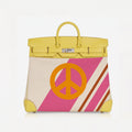 A structured yellow leather handbag with a front panel featuring a large orange peace sign over diagonal pink and cream stripes, shown on a clean white background.