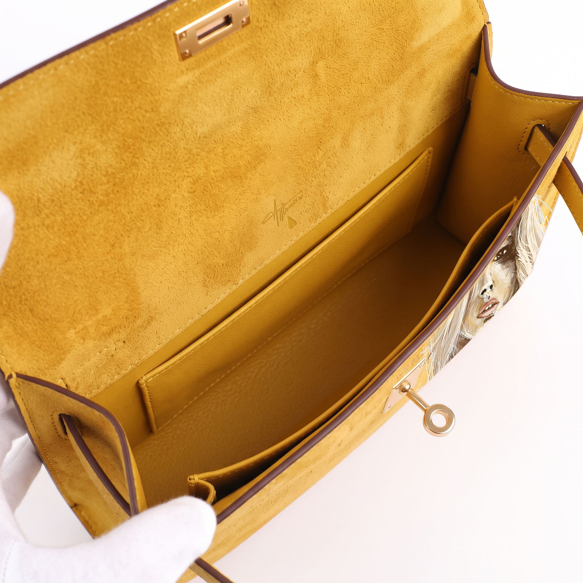 Crafted from luxurious yellow calfskin suede, the Kali Long clutch pochette combines a soft, velvety texture. Designed with a refined top handle, slim closure straps, and polished gold-tone twist-lock hardware, with front gorgeous art print, interior is beige suede with inside pocket