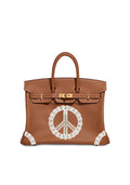 A brown leather handbag with gold-tone hardware and a large white lace peace sign appliqué on the front, shown against a plain white background.