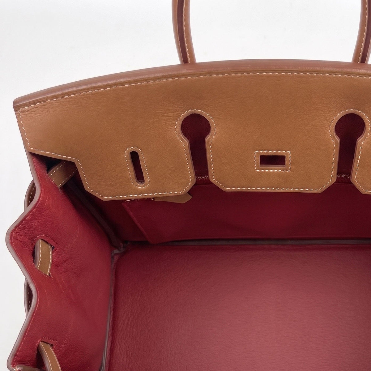 A top-down view of a luxury leather handbag, showing a tan exterior and a contrasting deep red interior lining. The brand name is embossed on the interior leather flap.