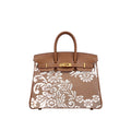 A structured brown leather handbag with a white floral lace overlay on the front, featuring gold-tone hardware and dual top handles, shown against a plain white background.