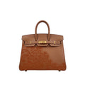 A brown leather handbag with a glossy embossed floral pattern on the lower front and gold-tone hardware, shown against a plain white background.