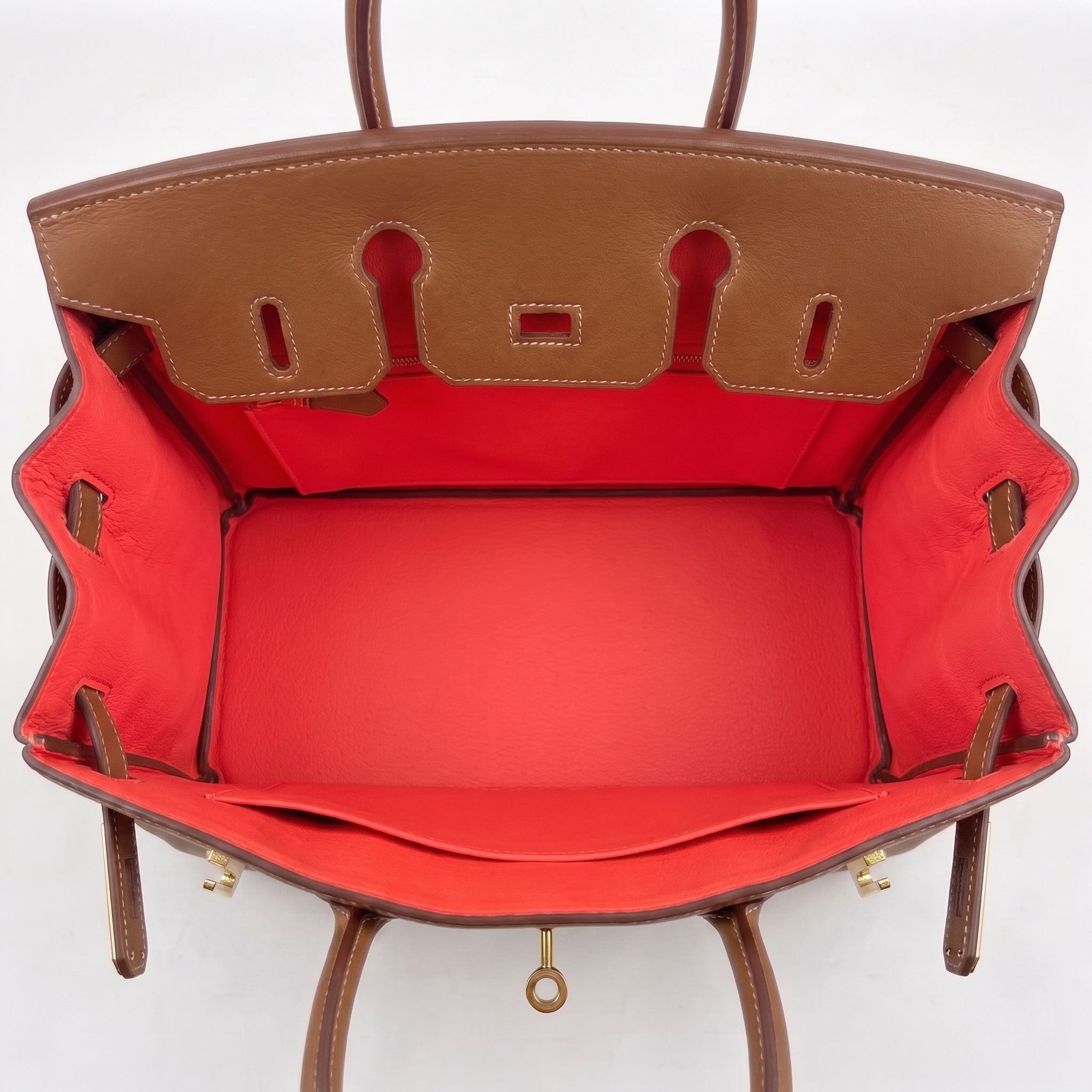 The interior of a structured leather handbag shown from above, featuring a warm brown leather exterior trim and a vibrant coral leather lining.