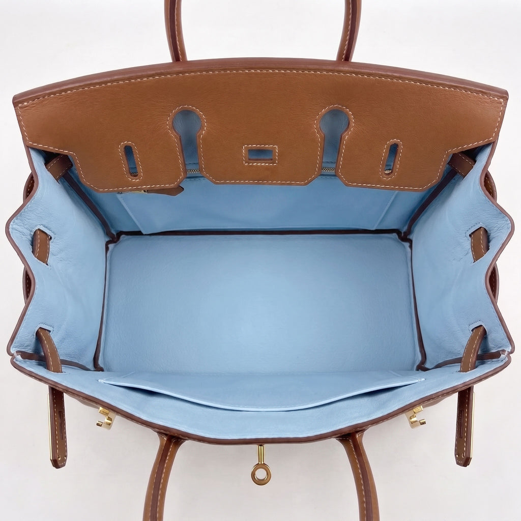 An open brown leather handbag shown from above, revealing a light blue satin interior lining with gold-tone hardware.
