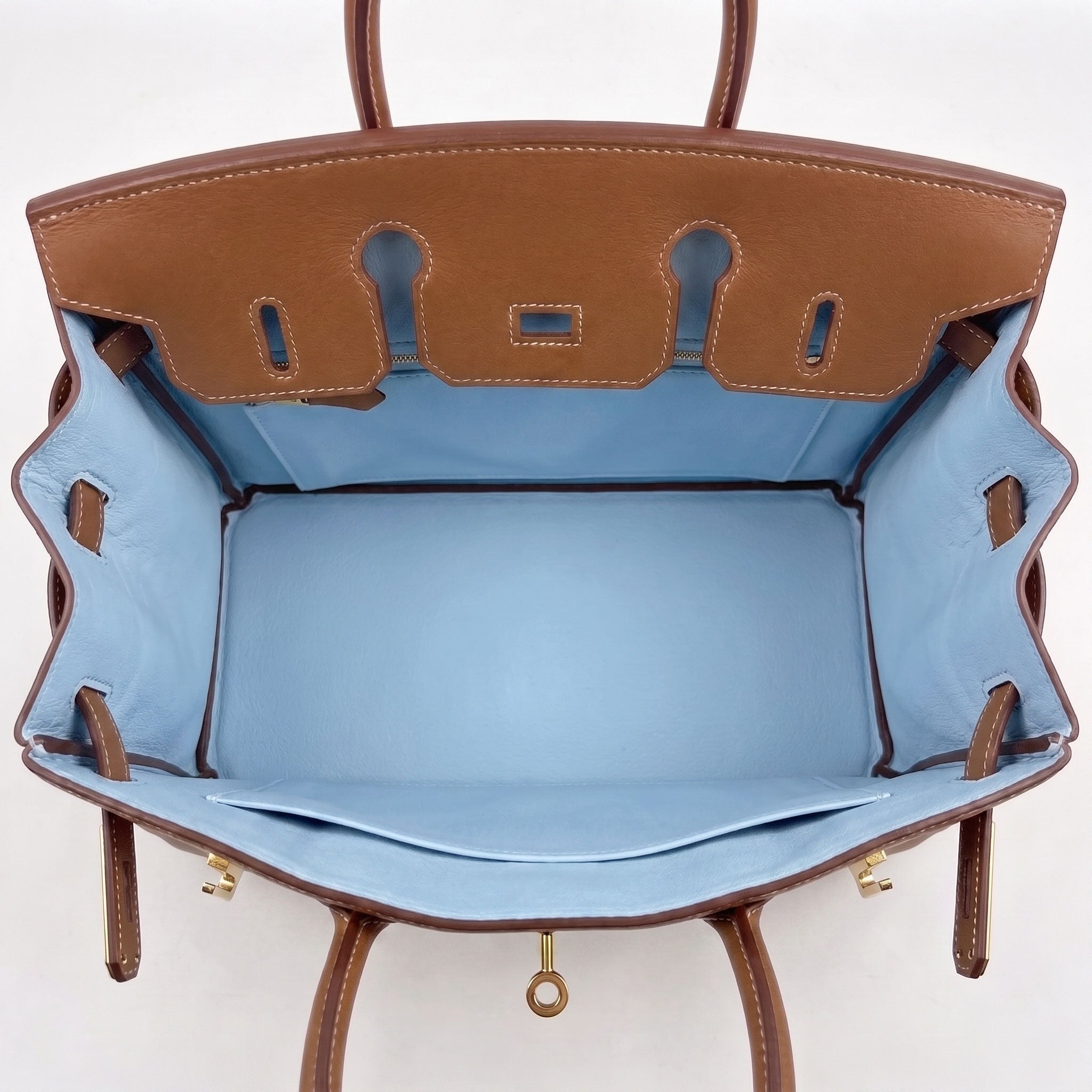 An open brown leather handbag shown from above, revealing a light blue satin interior lining with gold-tone hardware.