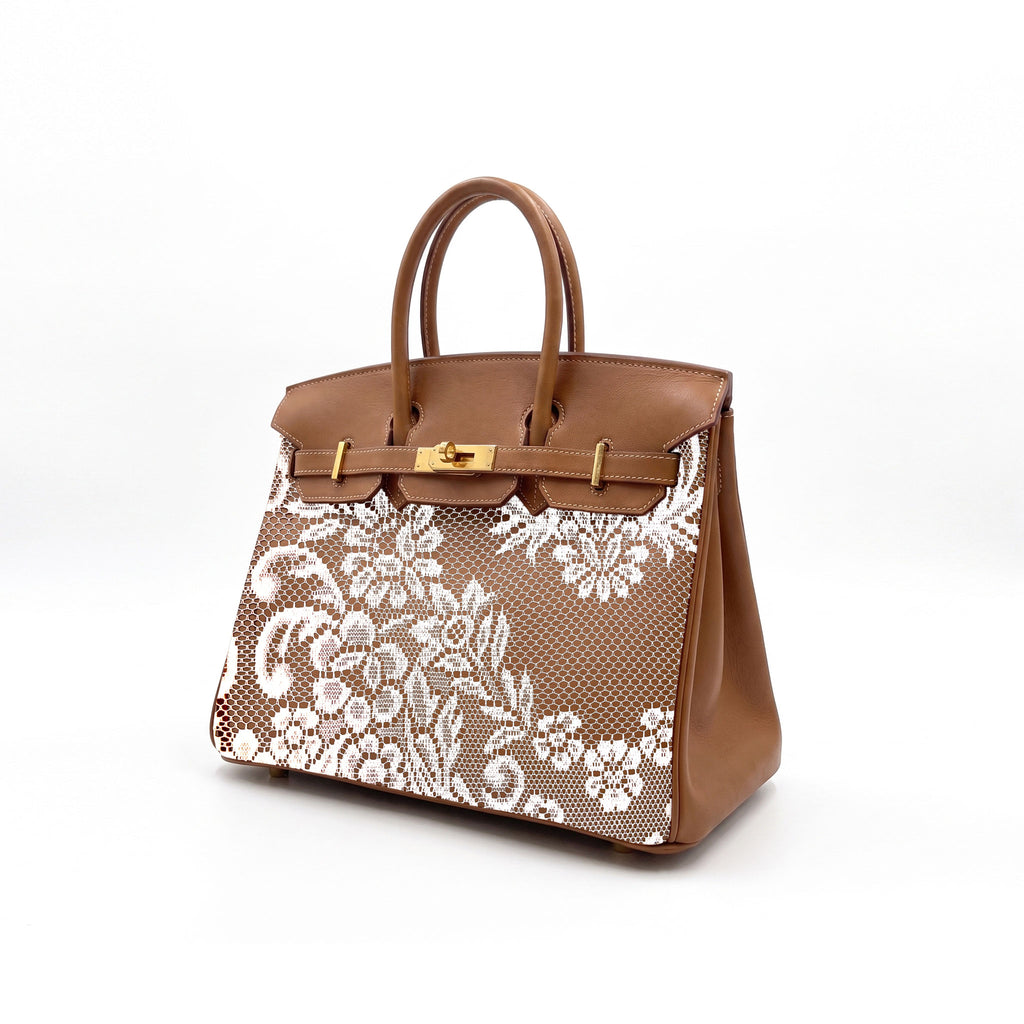 A brown leather handbag with a white floral lace overlay on the front, featuring gold-tone hardware and dual top handles, photographed on a clean white background.