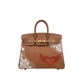 A brown leather handbag with gold-tone hardware, featuring a red embroidered winged heart on the front and white lace applique on the sides, shown against a plain white background.