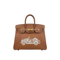 A brown leather handbag with gold-tone hardware and a white embroidered vintage car motif on the front, shown against a plain white background.