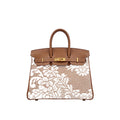 A structured top-handle handbag with tan leather trim and gold-tone hardware, featuring a white floral lace overlay on a tan woven body, shown against a plain white background.