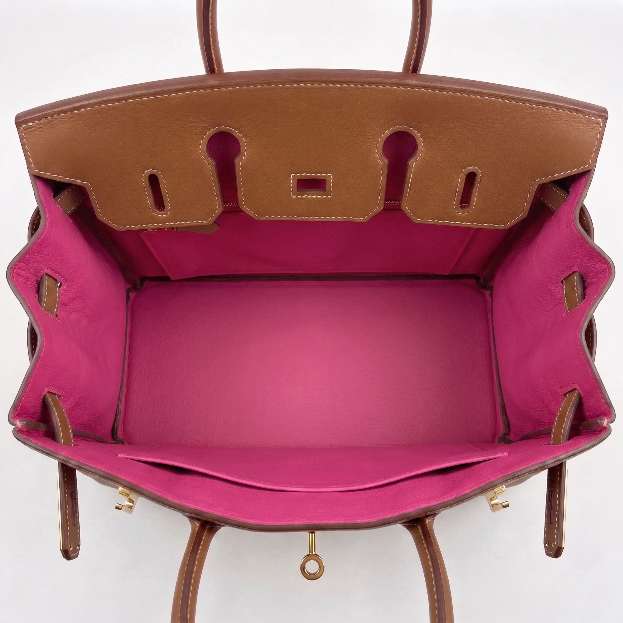 A luxury handbag shown from a top-down view, featuring a tan leather exterior with gold-tone hardware and a vibrant magenta pink interior lining.