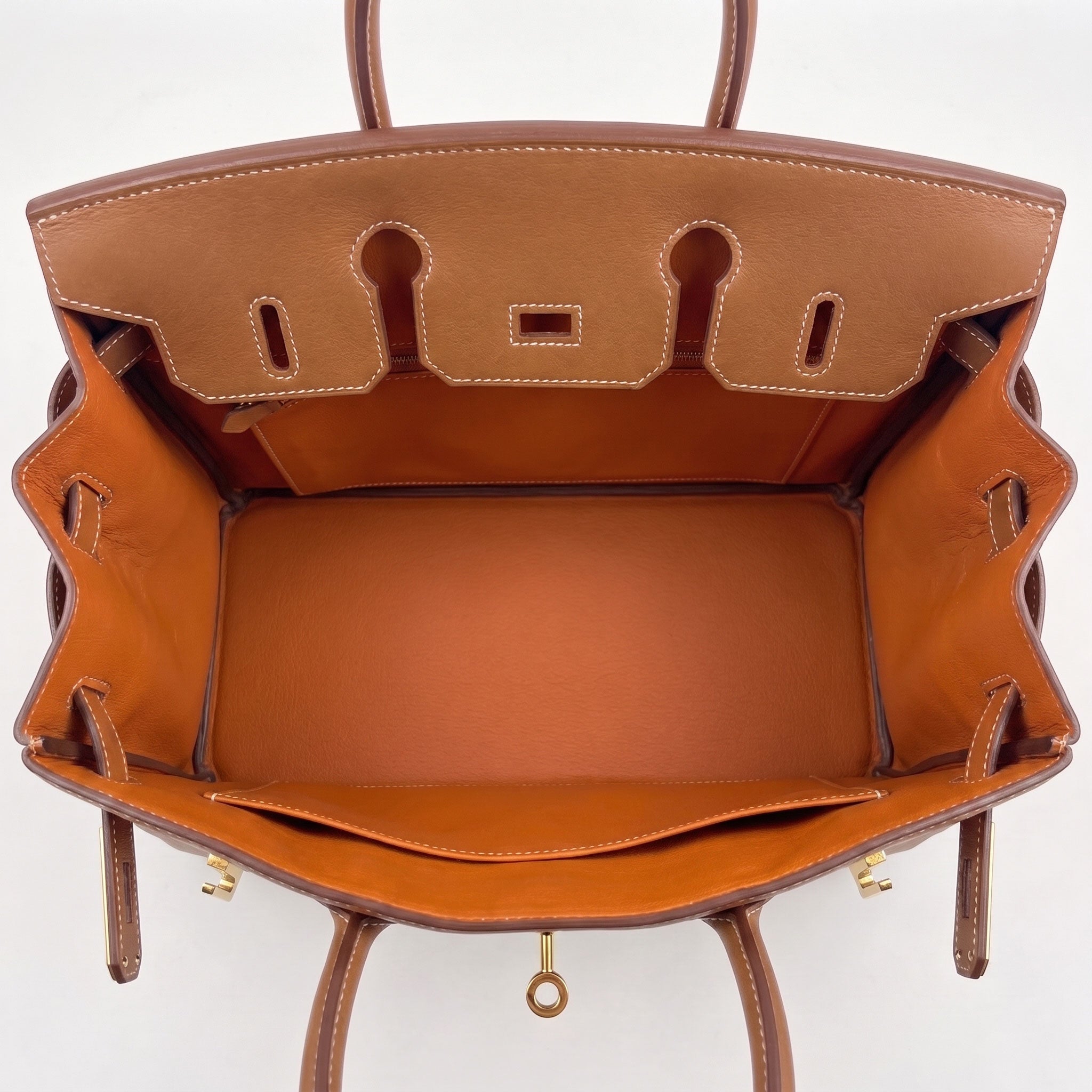 The interior of a tan leather handbag, photographed from above, showing the lined compartment, interior stitching, and top hardware against a plain white background.