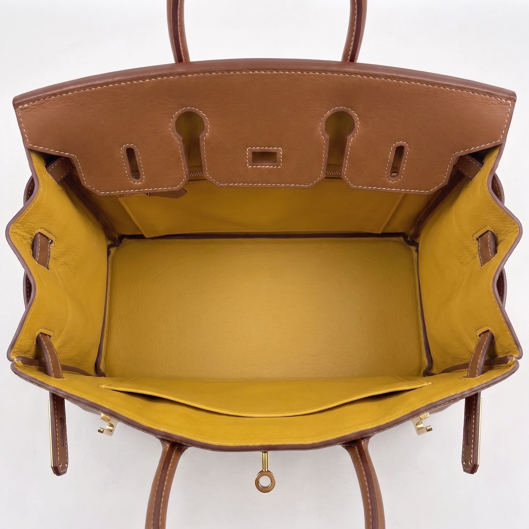 Top-down view of a brown leather handbag showing its mustard yellow interior lining and gold-tone hardware against a white background.