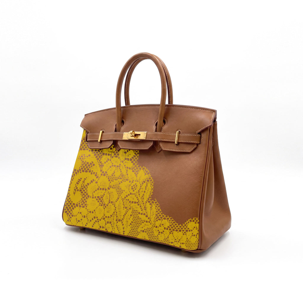 A structured brown leather handbag with a yellow print lace pattern on the front panel and gold-tone hardware, photographed on a clean white background.