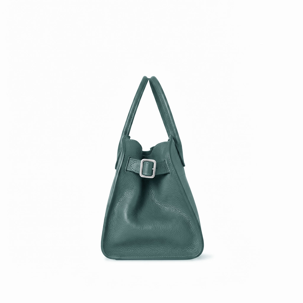 A dark teal green grained leather handbag with a structured slouchy silhouette, dual top handles, and a matching leather strap detail with a silver buckle on the front, shown against a plain white background.
