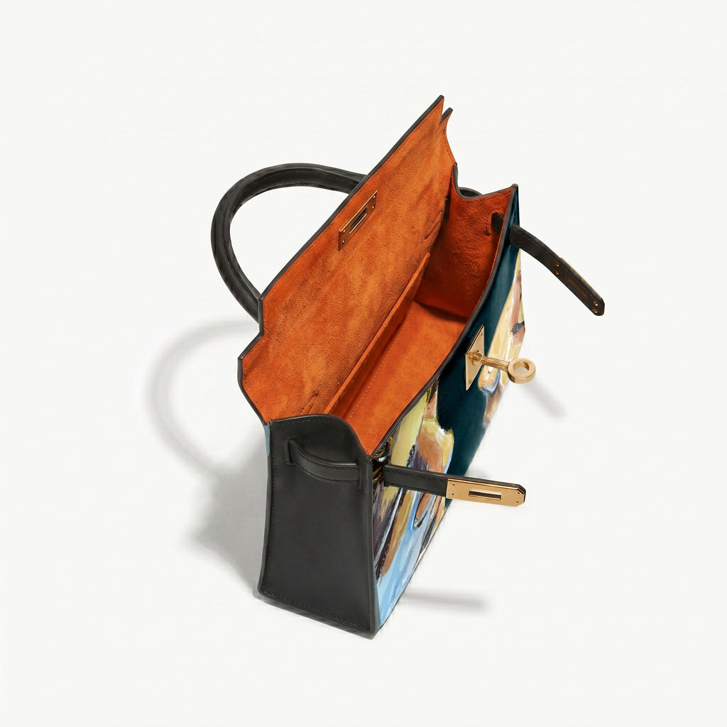 A structured leather handbag shown open from an elevated angle, featuring a black exterior, a warm orange suede interior, and a multicolor artistic print on the front panel with gold-tone hardware.