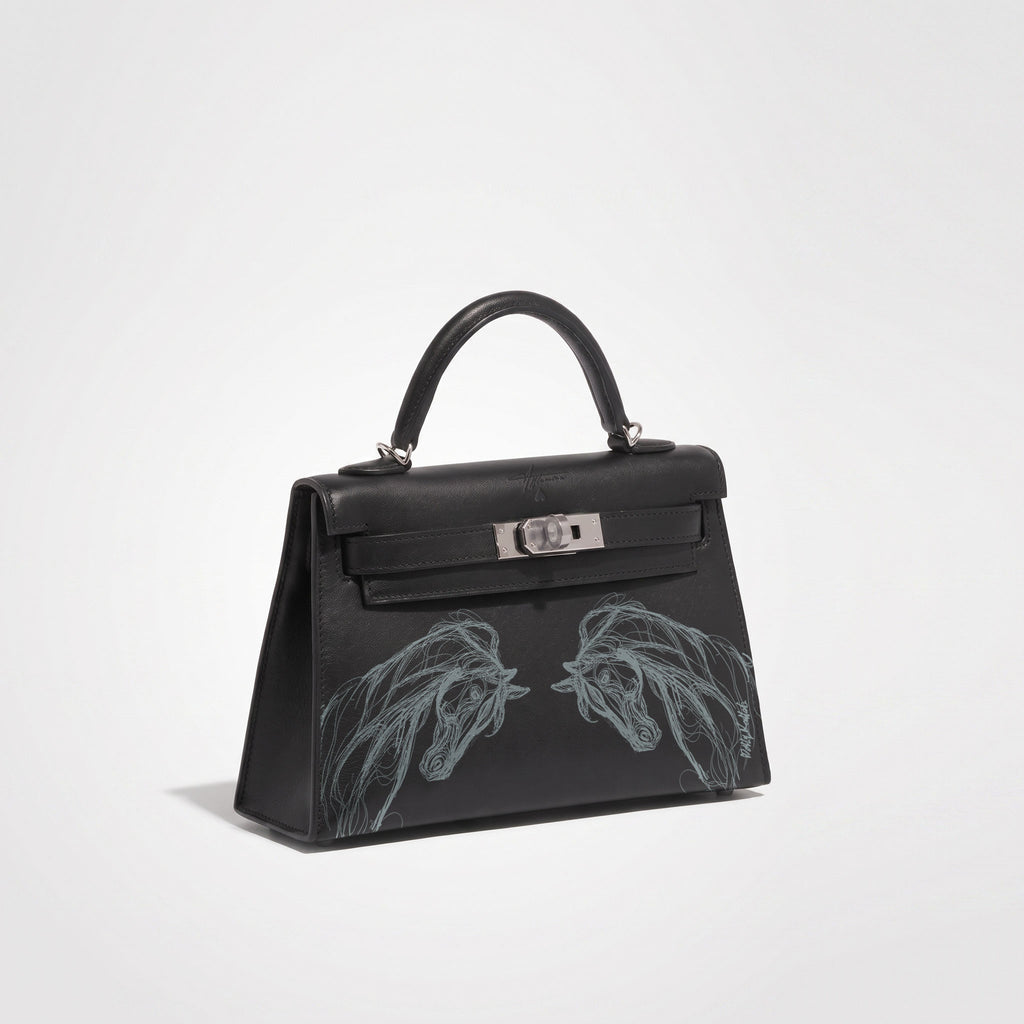 A black leather handbag with a top handle, silver-tone hardware, and two large silver line-art horse heads printed on the front, shown on a clean light gray studio background.