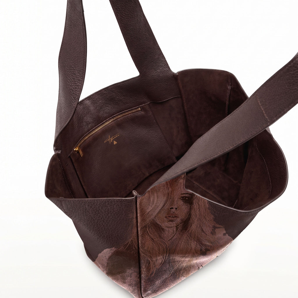 A dark brown leather tote bag with a printed portrait of a woman on the lower front panel and a zippered pocket inside, shown on a white background.
