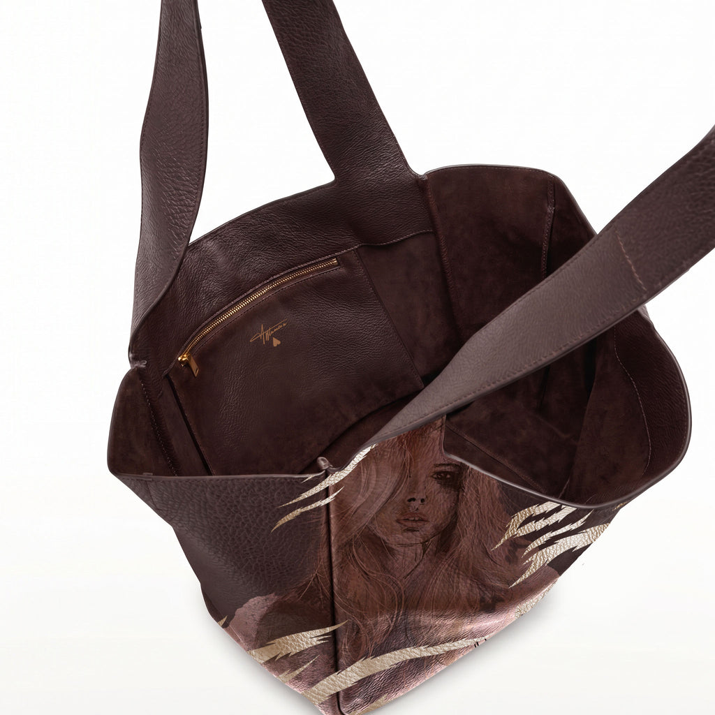 A dark brown leather tote bag with a printed illustration of a woman with long hair on the lower front panel, shown open against a white background.