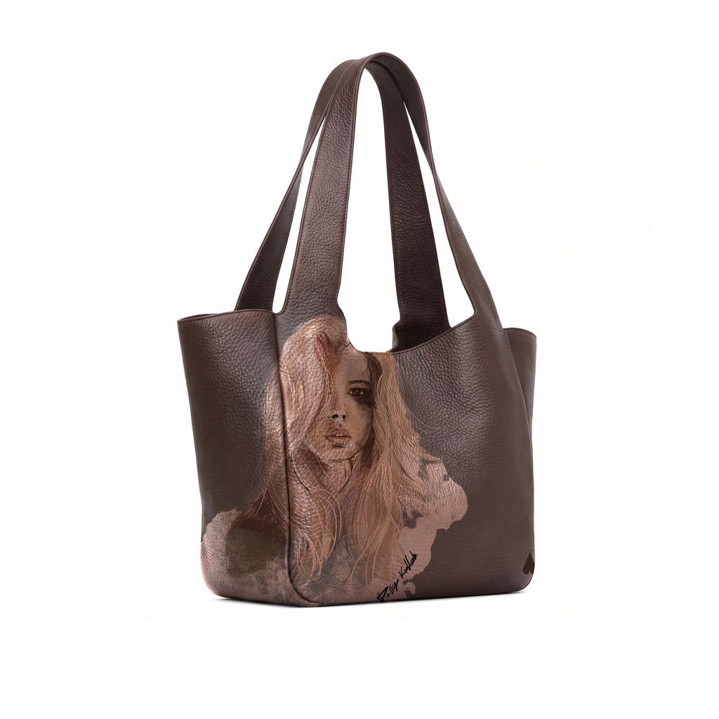 A dark brown full grained leather tote bag featuring a large, realistic portrait illustration of a woman with long blonde hair printed on the front, set against a plain white background.