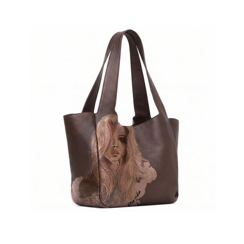 A dark brown leather tote bag with a printed portrait of a woman on the lower front panel and a zippered pocket inside, shown on a white background.